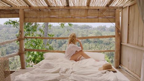 Mujer-Viajera-Sentada-En-La-Cama-En-Un-Hotel-Tropical-Disfrutando-De-Unas-Vacaciones-Relajándose-Cómodamente-Con-Vistas-Al-Paraíso-Selvático-Soñando-Despierta-Con-La-Próxima-Aventura