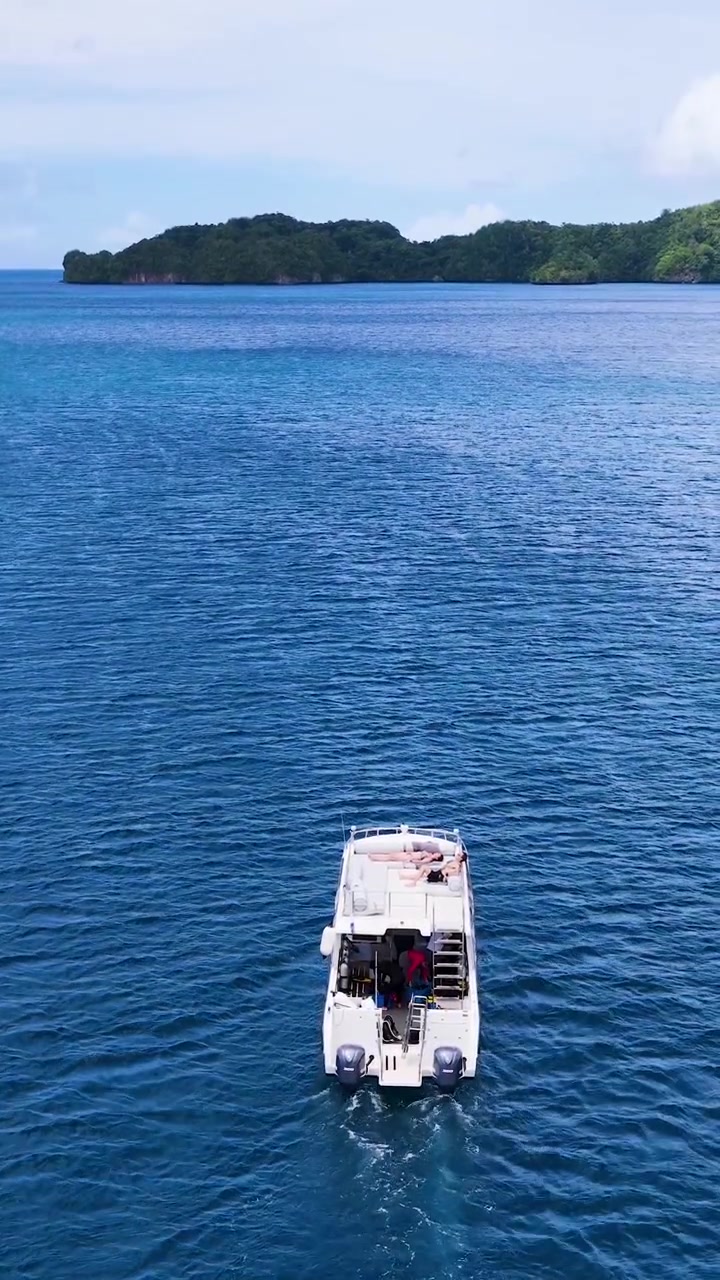 High angle drone shot follows a white motorboat traveling across deep blue tropical water
