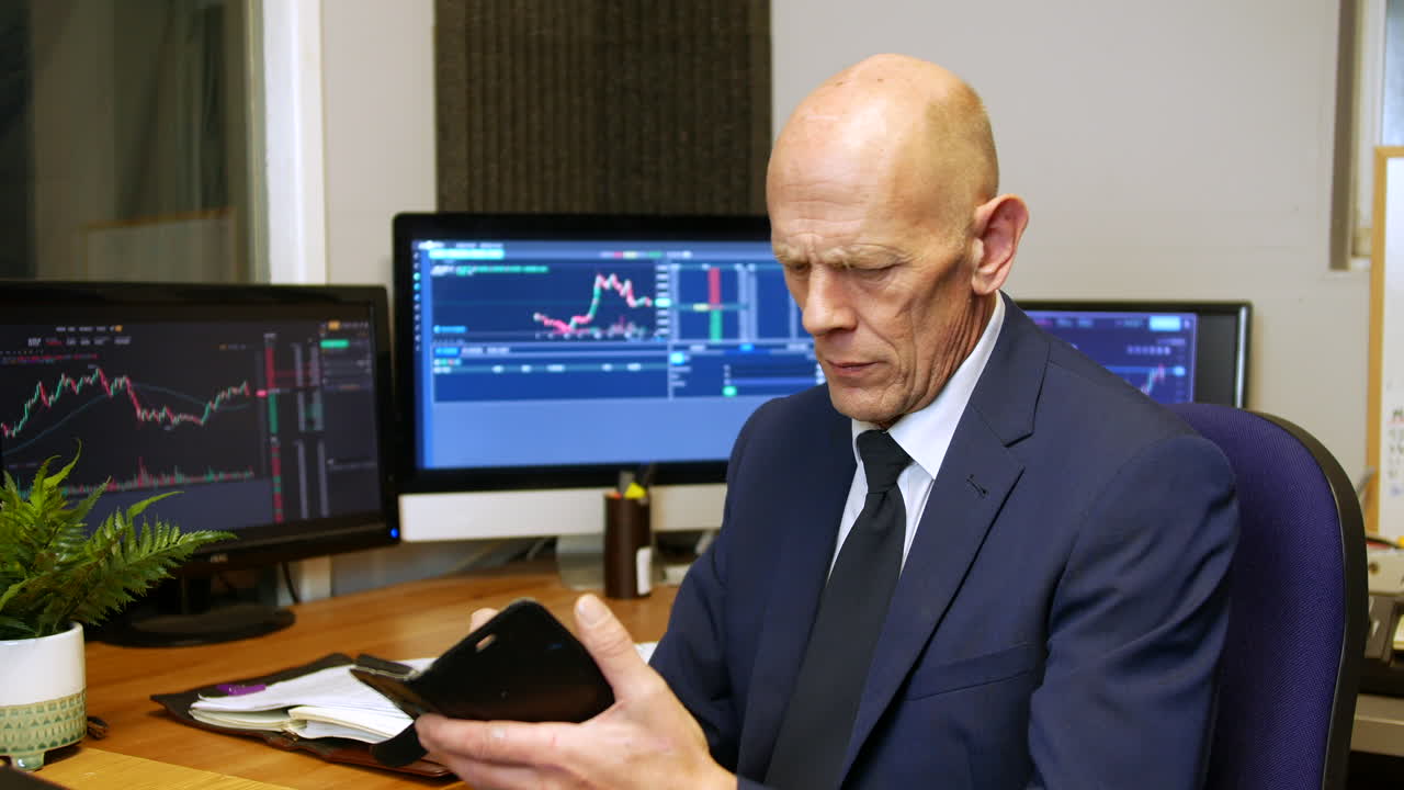A mature business man stock broker checking his phoneand messaging in his trading office