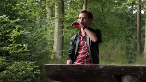 young adult man having break during hiking in forest to drink by wooden table