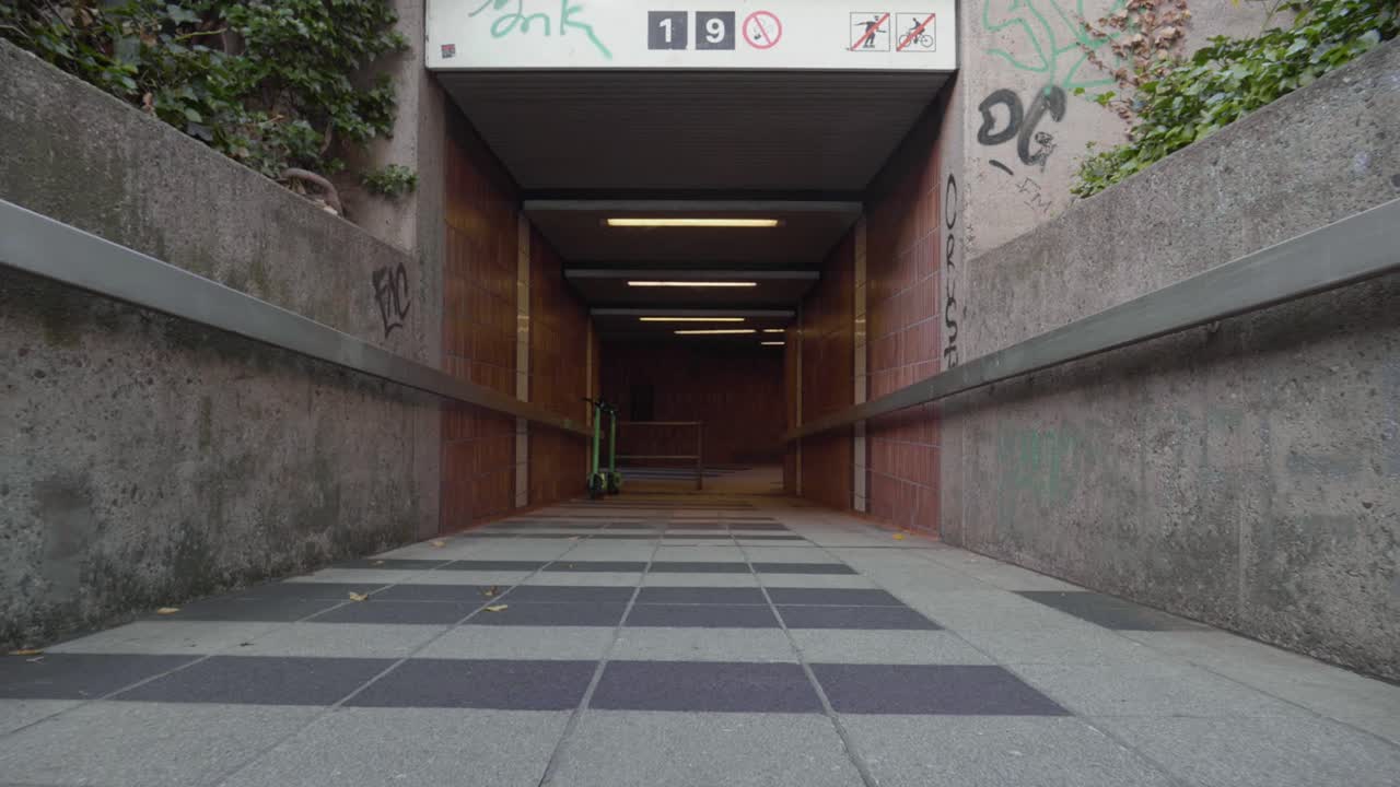 tiro bajo del carro hacia adelante entrando en un túnel de la estación de metro con graffiti en las paredes y scooters eléctricos listos para usar