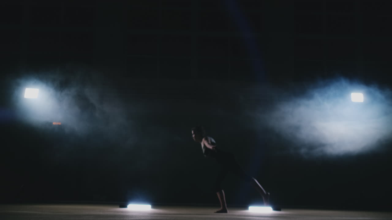 In slow motion in the smoke girl acrobat performs several back flips and coups in the air. Training acrobatic performance. Women's gymnastics competitions.