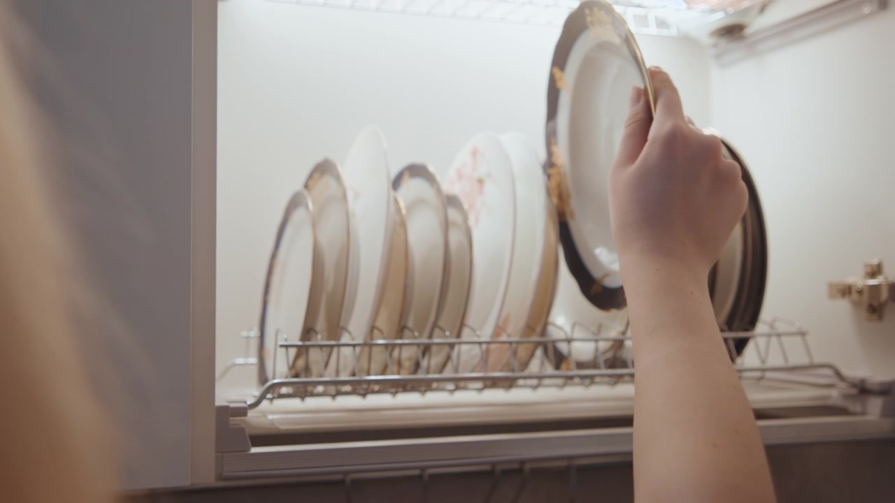 Organisering af køkkenservice. Forsigtig placering af porcelænstallerkener. Blide hænder arrangerer fint keramik. Ryddeligt køkken med omhyggeligt opbevarede porcelænstallerkener efter madlavning.