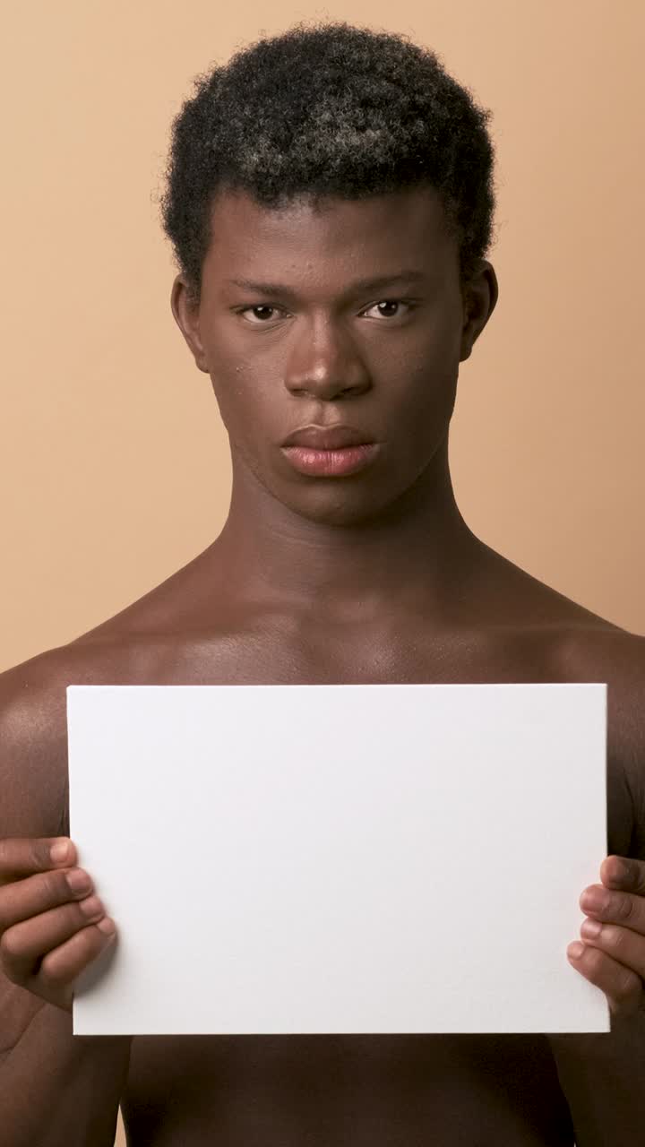 Persona transgender africana seria che tiene in mano un poster bianco.