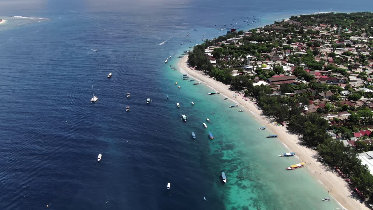 Aerial pullback view of sunny Gili Trawangan beach with boats resting in the calm turquoise water