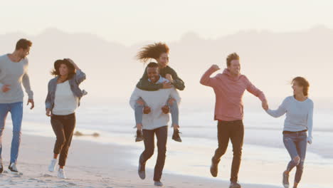 Gruppe-Von-Freunden,-Die-Spaß-Daran-Haben,-Gemeinsam-Am-Winterstrand-Entlang-Zu-Laufen