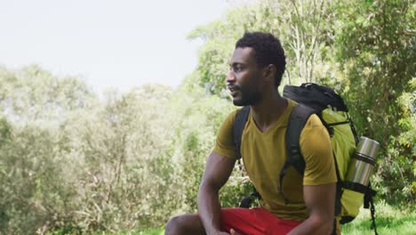 Fröhlicher-Afroamerikanischer-Mann-Mit-Rucksack-Sitzt-Im-Park,-Zeitlupe