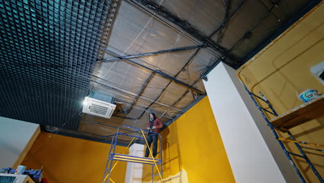 spacious room with yellow walls and white columns. men work in the room mending and installing the light on the ceiling. low angle view.