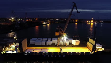 shipping containers being loaded on a cargo vessel at night with a crane - ascending aerial view