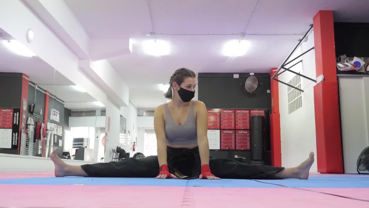 Woman with facemask trains and warms up for boxing training with a split
