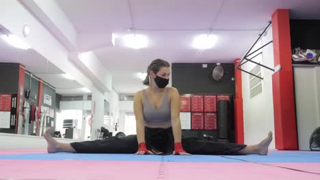 woman with facemask trains and warms up for boxing training with a split
