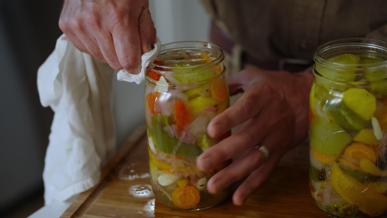 Closeup view of chef handling pickled vegetables and wiping the liquids on mouth of jar using a cotton cloth.