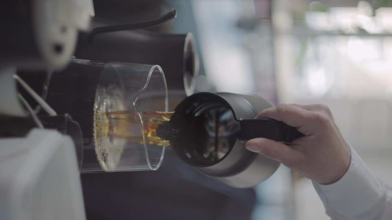 Vertical, insulated pot pours coffee into clear glass carafe at coffee shop