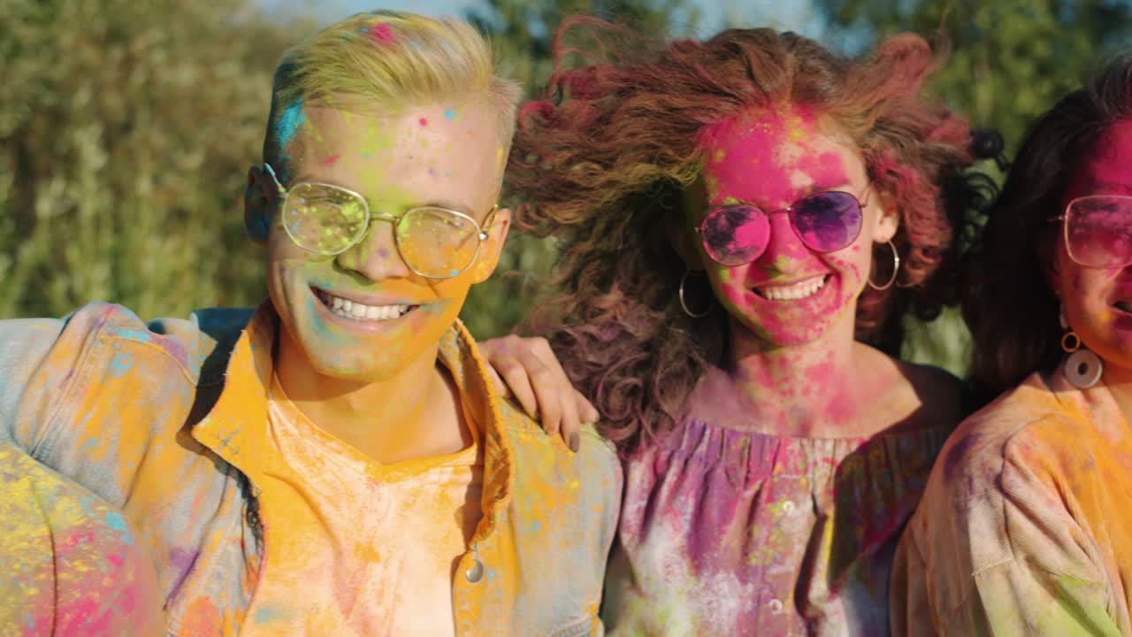 Portrait of happy young people friends covered with powder paint standing together at Holi festival