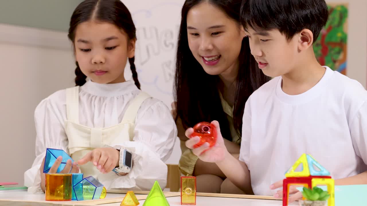 2人の子供と先生が協力して、教室でSTEMブロックを使ってカラフルな幾何学的構造を構築している。