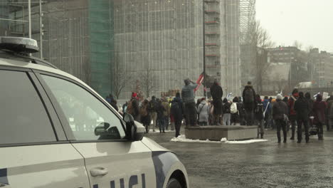 Menschen,-Die-An-Einem-Kalten-Regnerischen-Tag-Auf-Einem-Platz-Zwischen-Hohen-Gebäuden-Gegen-Covid-beschränkungen-Und-Allgemeine-Pandemiepolitik-In-Helsinki-Protestieren