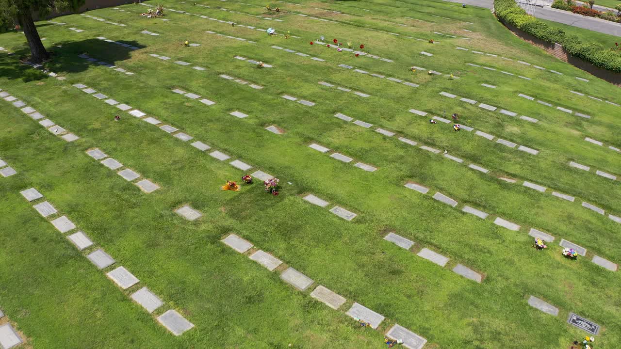 una toma aérea descendente y inclinada hacia arriba de un césped funerario con filas de lápidas decoradas con flores en una funeraria de california