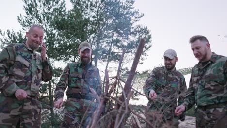 conversación de soldados en ropa de camuflaje, están discutiendo por la noche junto a la fogata común fritando salchichas para la cena, los hombres están descansando después del trabajo, servicio, ejercicios de campo