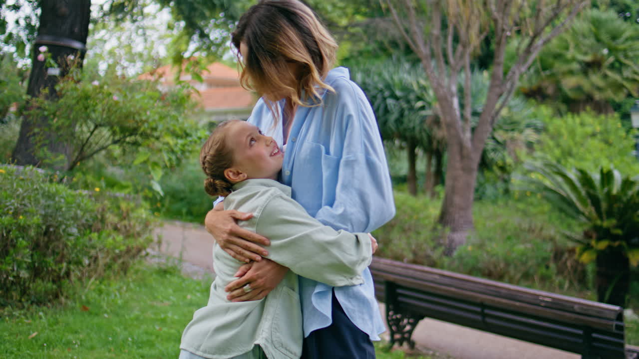 Loving mom cuddling kid in greenery park resting together. Mother embracing girl
