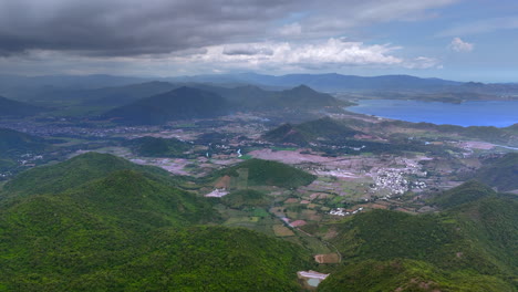 tomada por avión no tripulado de west sumbawa, un vasto paisaje de colinas verdes, valles y asentamientos dispersos bajo un cielo nublado, con una vista lejana del océano azul y el fondo montañoso