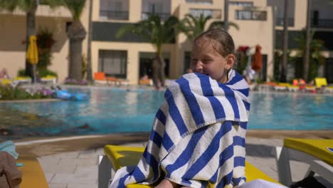 girl teenager wrapping in towel sitting deckchair on swimming pool background