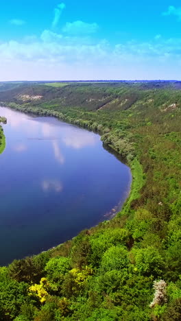 view of the countryside with houses, fields and trees which are surrounded by wide river on the background of high rocks. aerial view. vertical video
