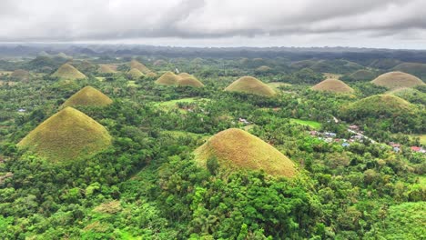 aerial landscape of the chocolate hills in bohol, philippines, where hundreds of cone-shaped grass hills rise from a dense tropical forest, creating a stunning natural terrain beneath a cloudy sky