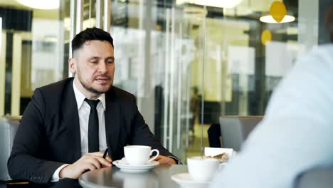 cheery caucasian businessman gesticulating and rejoicing in buisness profits while talking to his partner in mod cafe during lunch.