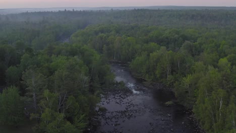 remnants of setting sun in distance beyond river flowing through dense wilderness