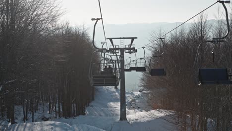 Ski-lift-moving-over-snowy-landscape-between-leafless-trees,-ski-resort