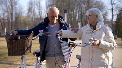 senior couple holding bikes while walking and talking in the park on a winter day