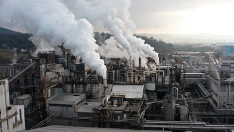 industrial factory emitting thick white smoke from multiple chimneys under a cloudy sky