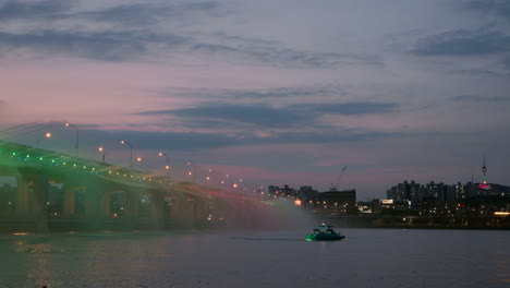 Farbenfrohe-Skyline-Von-Seoul-In-Der-Nähe-Der-Banpo-Brücke,-Regenbogenbrunnen-In-Der-Dämmerung-Bei-Sonnenuntergang-Mit-Patrouillenboot-Am-Han-Fluss-Und-Beleuchtetem-Namsan-Turm