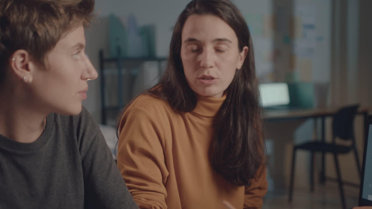 Female Coworkers Discussing Presentation on Laptop during Night Office Meeting