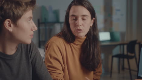 female coworkers discussing presentation on laptop during night office meeting