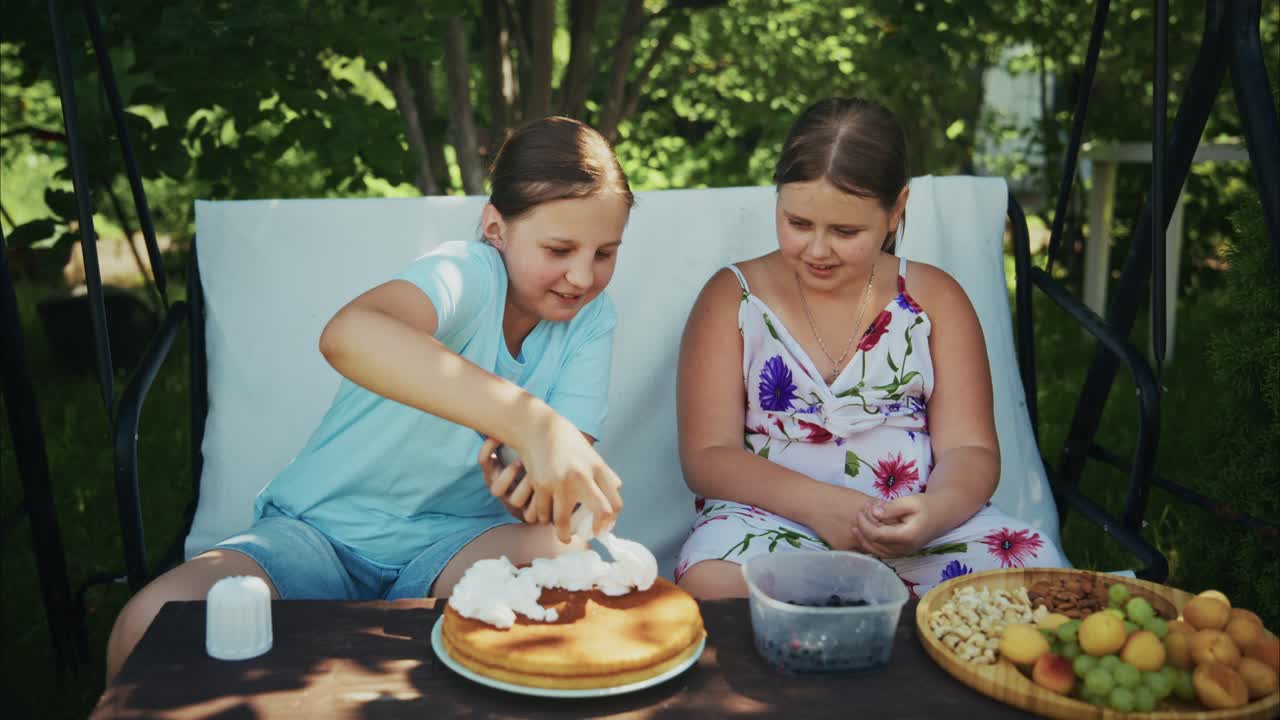Two girls enjoying dessert outdoors, one decorating cake with cream, surrounded by fresh fruits