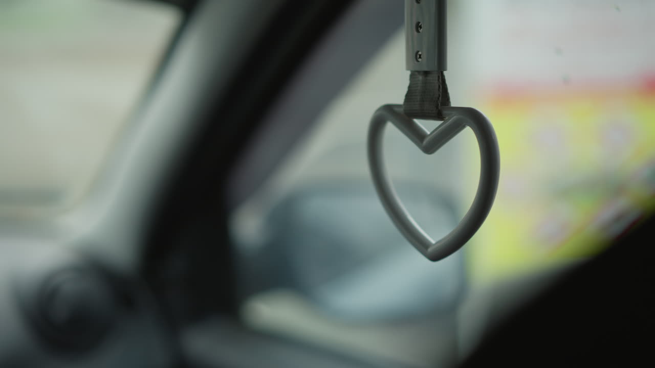 Side view inside moving car showing heart shaped handle swinging by passenger seat window with blurred urban background during winter commute capturing subtle motion and cabin detail