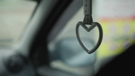 side view inside moving car showing heart shaped handle swinging by passenger seat window with blurred urban background during winter commute capturing subtle motion and cabin detail