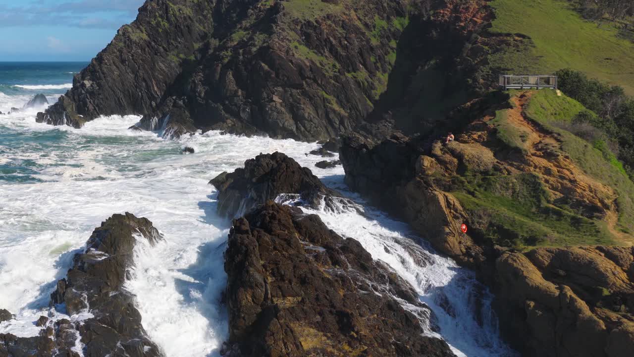Dynamic aerial view of waves hitting rocky cliffs at Byron Bay, Australia. Bright daylight enhances the vibrant coastal scenery