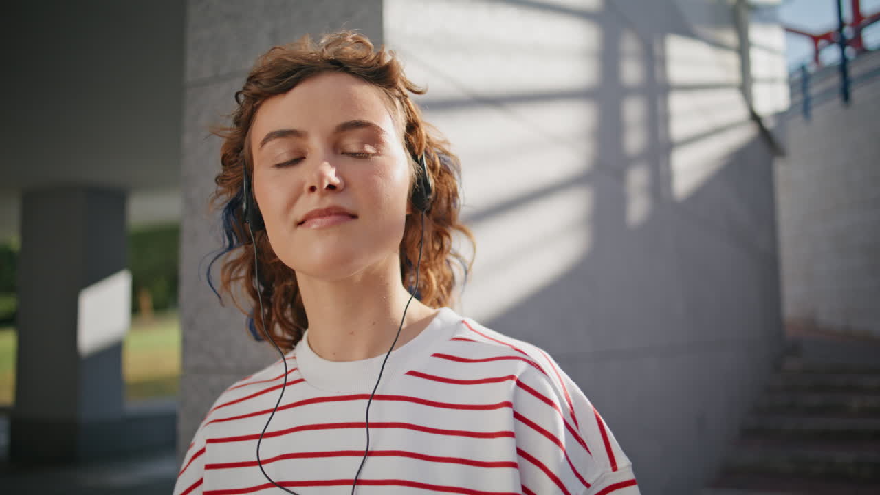 elegante hipster escuchando auriculares música cerrando los ojos en la calle soleada de cerca