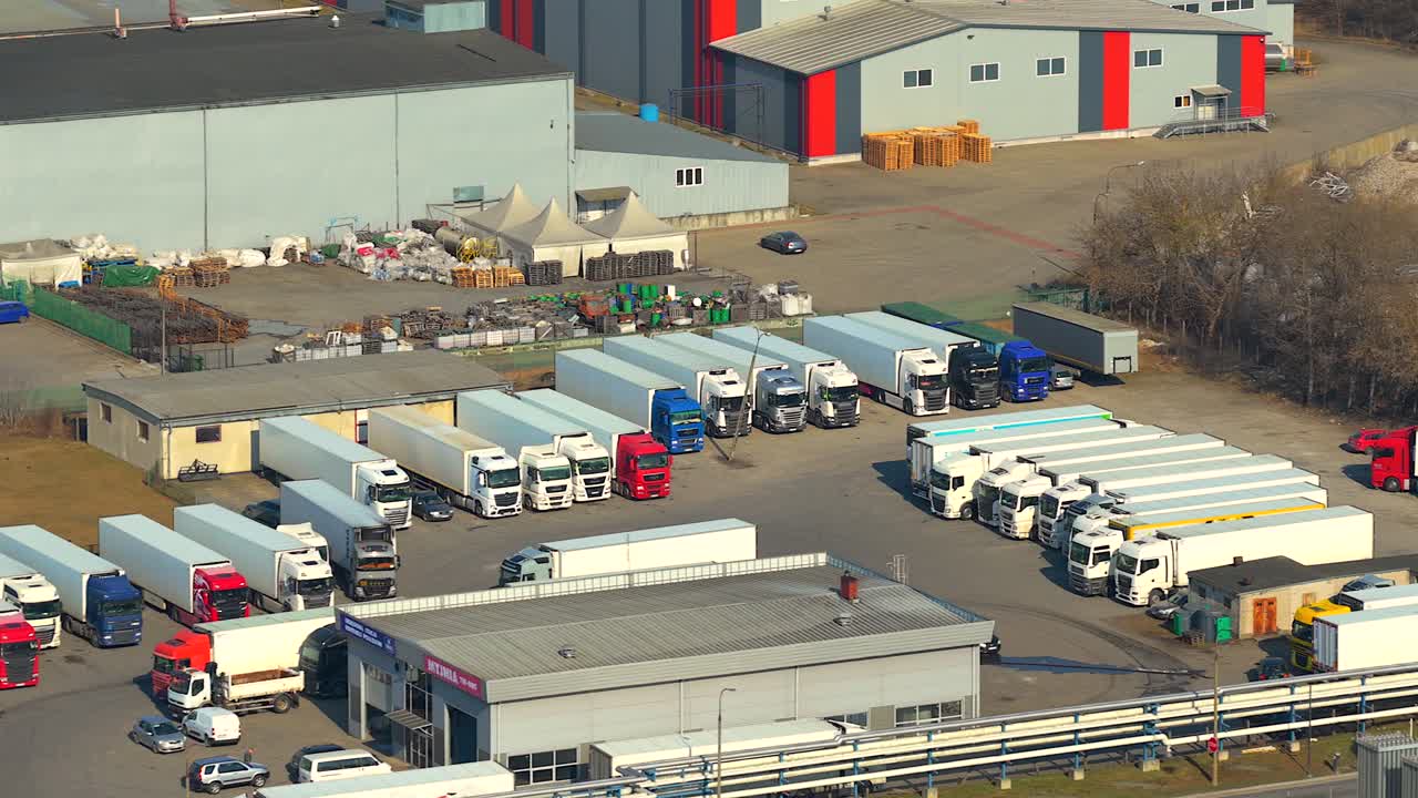 Oversigtsbillede af en stor parkeringsplads med mange farverige sættevogne parkeret ved et logistikknudepunkt i et industriområde i Grajewo, Polen.