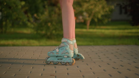 side leg view of person roller skating on interlocked path, wearing teal rollerblades, shadow cast on ground, next to grassy field, blurred background of greenery