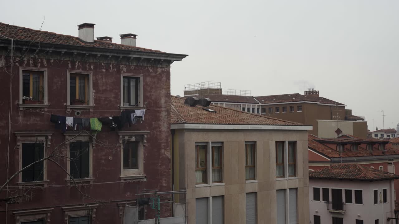 A clothesline full of drying laundry is visible on a classic Venetian residential building, set against an urban backdrop.