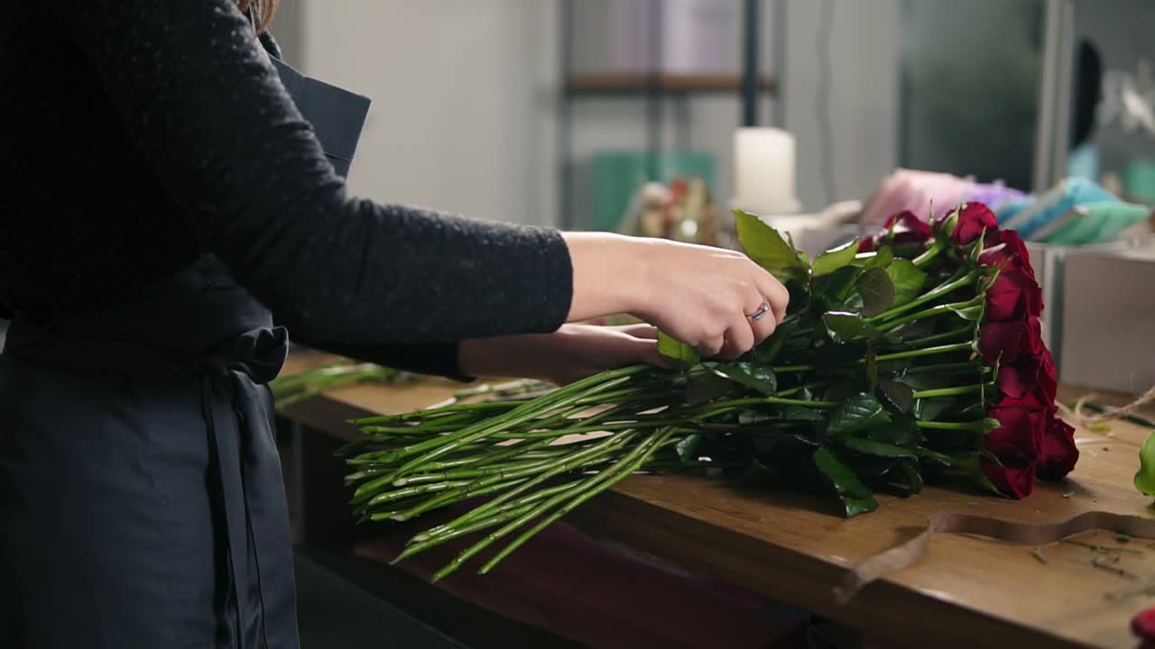 Close Up view of hands of female florist arranging modern bouquet using beautiful red roses at flower shot. Slow Motion shot