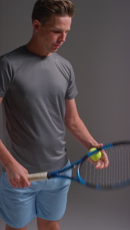 una toma de estudio de video vertical de un jugador de tenis masculino sosteniendo una raqueta y una pelota rebotando disparada contra un fondo gris