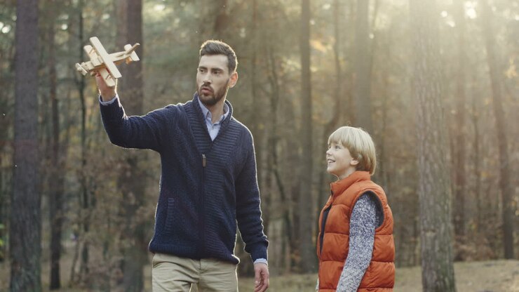Caucasian handsome man playing with his little cute son with a wooden plane in the forest