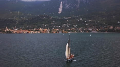 Velero-En-El-Lago-Di-Garda-Con-Acantilados-De-Garda-Al-Fondo-En-Un-Día-Parcialmente-Nublado