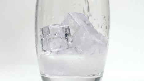 ice cubes falling into glass and then filled with soda or sparkling water slow motion close up product studio slow motion