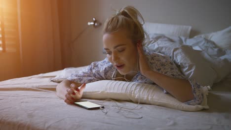 charming young woman with ponytail listening to good music while lying on comfortable bed