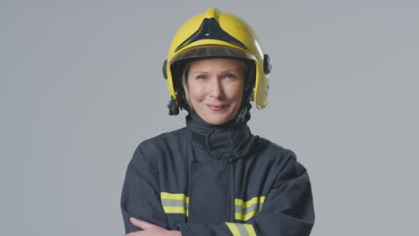 studio portrait of smiling mature female firefighter wearing helmet against plain background